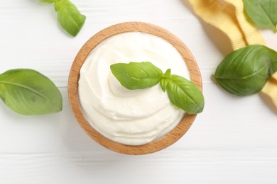 Photo of Delicious yogurt in bowl and basil on white wooden table, flat lay