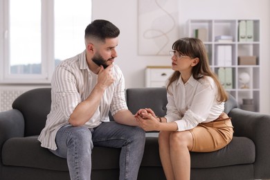 Photo of Psychologist supporting patient during therapy session on sofa in office