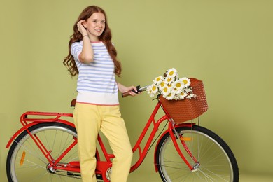 Photo of Smiling teenage girl and bicycle with basket of flowers against green background