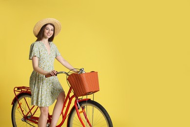 Photo of Smiling woman in hat posing on bicycle with basket against light green background. Space for text