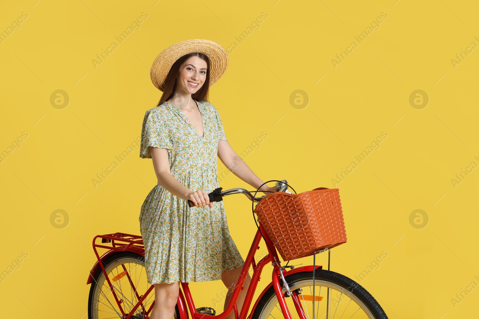 Smiling woman in hat riding bicycle with basket against light green background Photo of Smiling woman in hat riding bicycle with basket against light green background