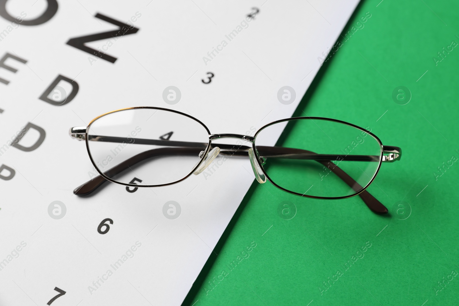 Photo of Vision test chart and glasses on green background, above view