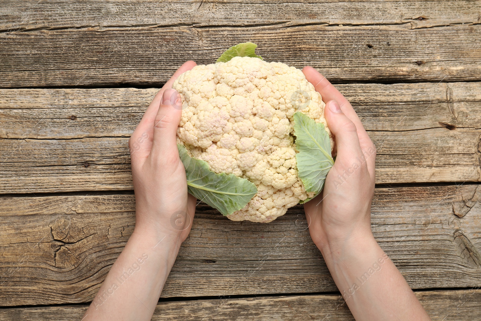 Woman with whole cauliflower at wooden table, top view Photo of Woman with whole cauliflower at wooden table, top view