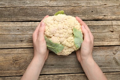 Photo of Woman with whole cauliflower at wooden table, top view