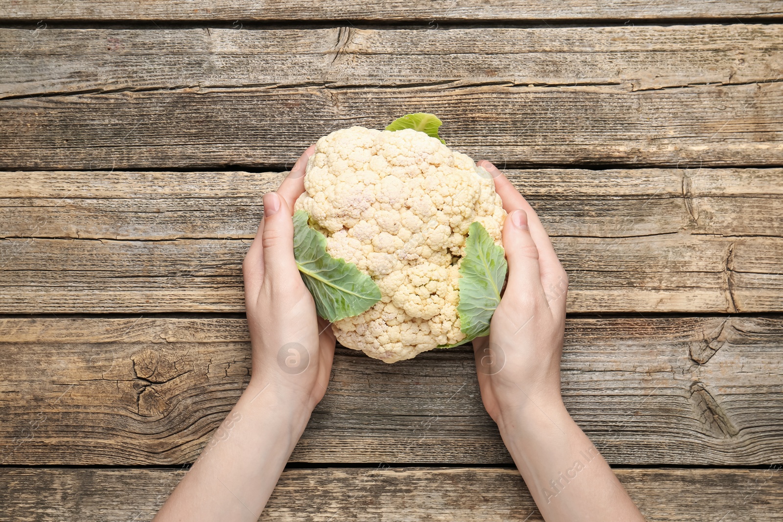 Woman with whole cauliflower at wooden table, top view Photo of Woman with whole cauliflower at wooden table, top view