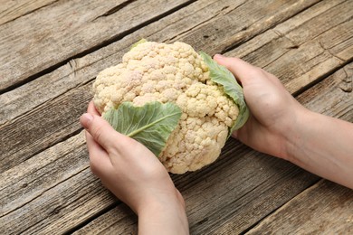 Photo of Woman with whole cauliflower at wooden table, closeup