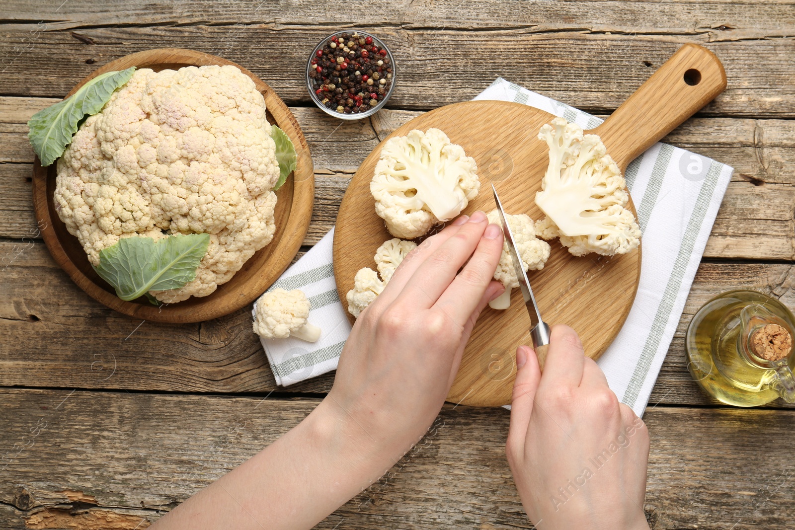 Photo of Woman cutting raw cauliflower at wooden table, top view