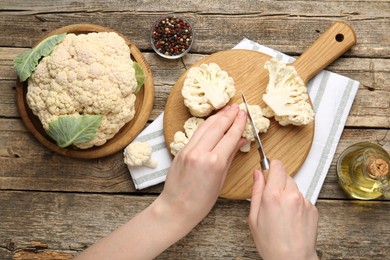 Photo of Woman cutting raw cauliflower at wooden table, top view