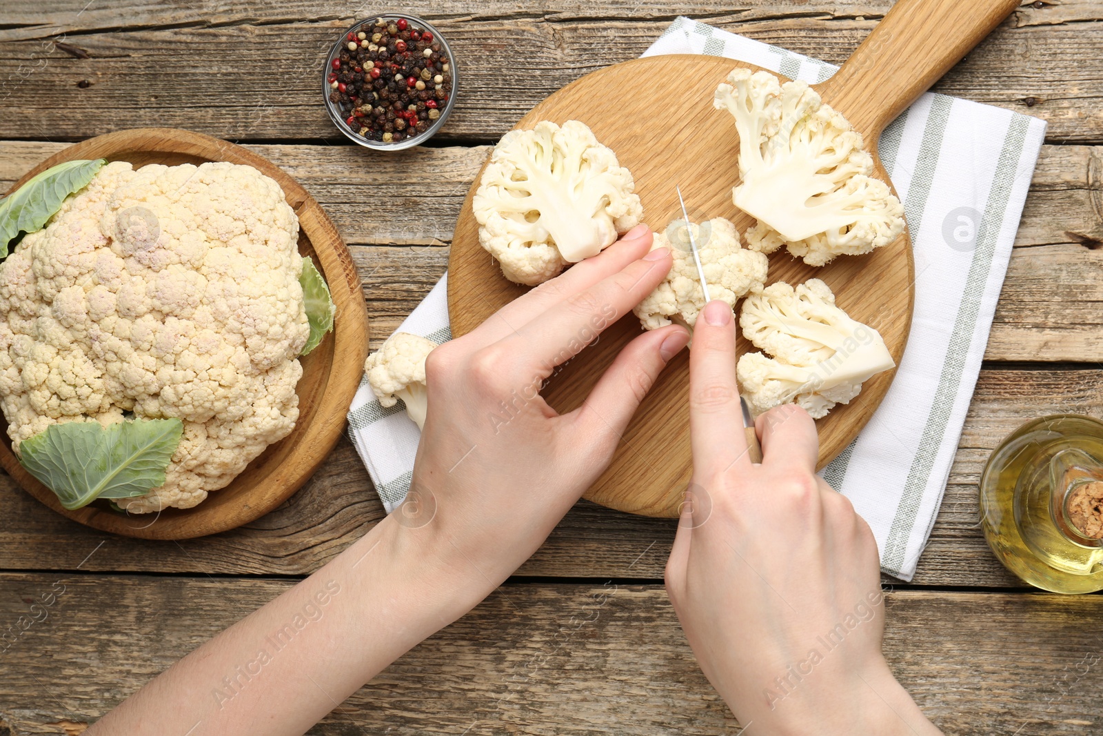 Photo of Woman cutting raw cauliflower at wooden table, top view
