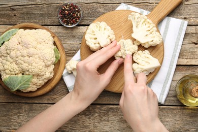 Photo of Woman cutting raw cauliflower at wooden table, top view