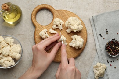 Photo of Woman cutting raw cauliflower at light table, top view