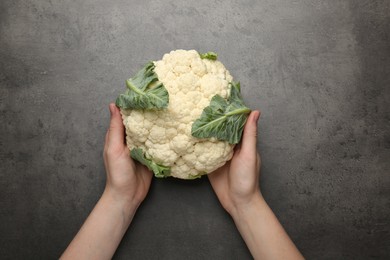 Photo of Woman with whole cauliflower at grey table, top view