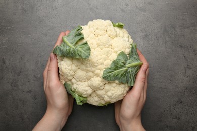 Photo of Woman with whole cauliflower at grey table, top view