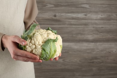 Photo of Woman with whole cauliflower on wooden background, closeup. Space for text