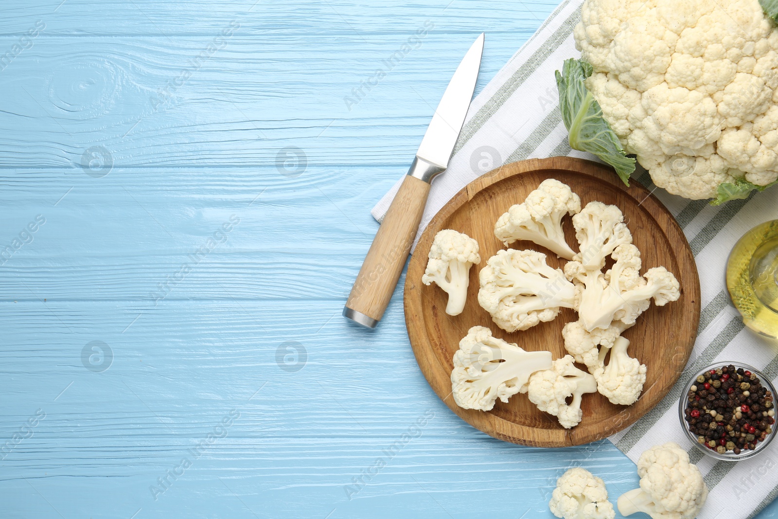 Pieces of cauliflower, peppercorns, oil and knife on light blue wooden table, flat lay. Space for text Photo of Pieces of cauliflower, peppercorns, oil and knife on light blue wooden table, flat lay. Space for text