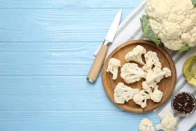 Photo of Pieces of cauliflower, peppercorns, oil and knife on light blue wooden table, flat lay. Space for text