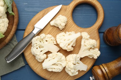 Photo of Pieces of cauliflower, knife and spices on blue wooden table, flat lay
