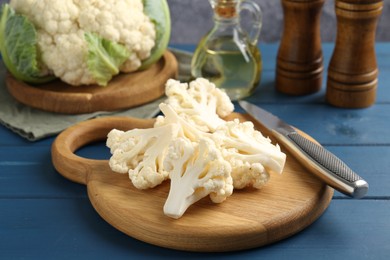 Photo of Pieces of cauliflower, knife and spices on blue wooden table, closeup