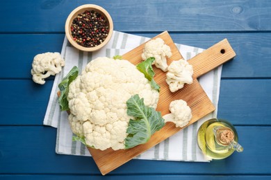 Photo of Raw cauliflower, peppercorns and oil on blue wooden table, flat lay