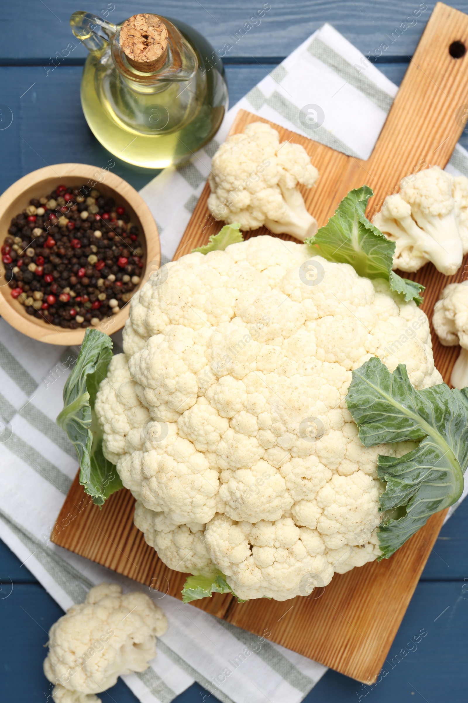 Raw cauliflower, peppercorns and oil on blue wooden table, flat lay Photo of Raw cauliflower, peppercorns and oil on blue wooden table, flat lay