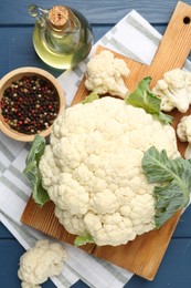 Photo of Raw cauliflower, peppercorns and oil on blue wooden table, flat lay