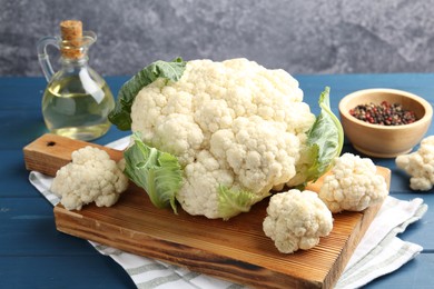 Photo of Raw cauliflower, peppercorns and oil on blue wooden table