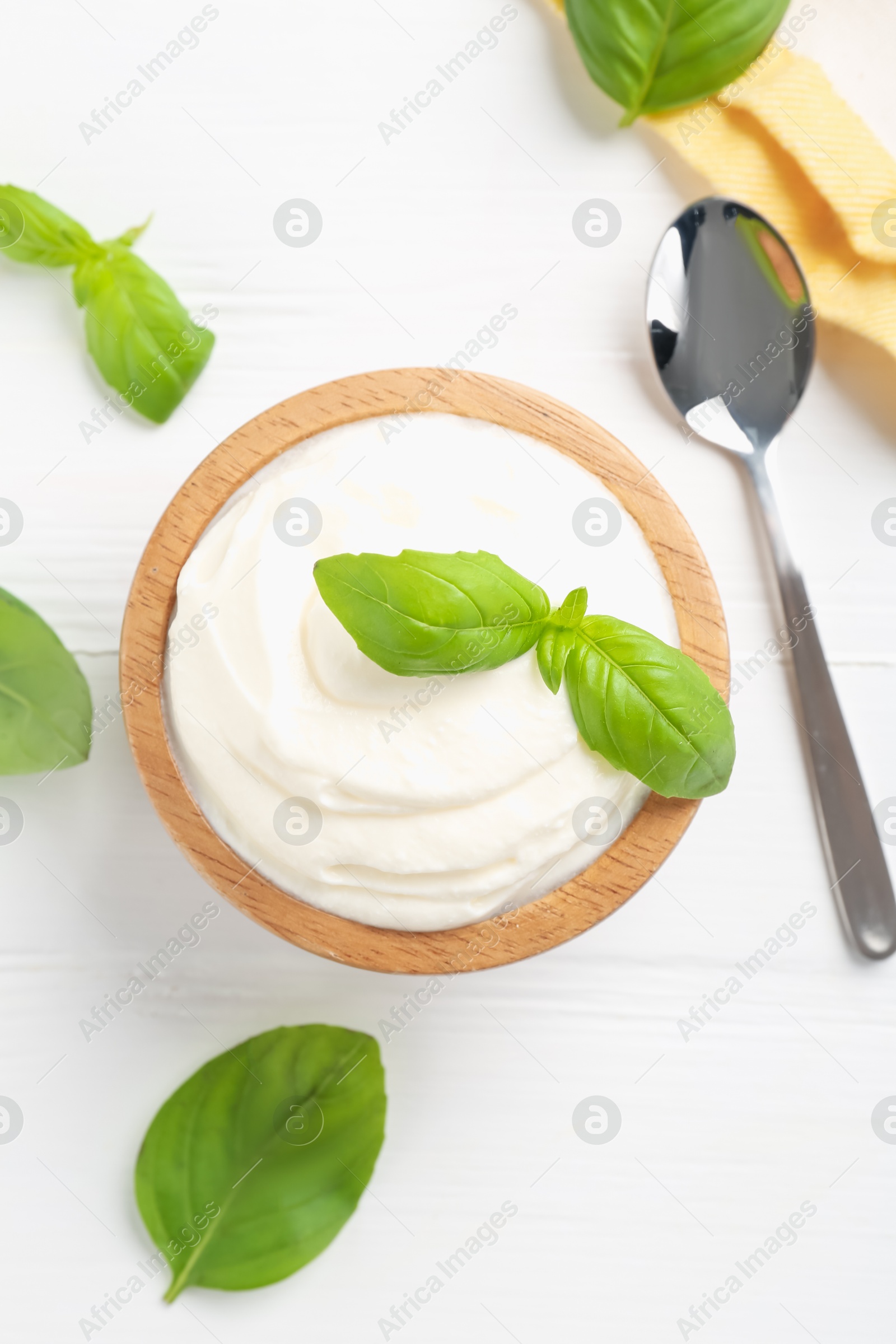 Delicious yogurt in bowl, basil and spoon on white wooden table, flat lay Photo of Delicious yogurt in bowl, basil and spoon on white wooden table, flat lay