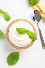 Photo of Delicious yogurt in bowl, basil and spoon on white wooden table, flat lay
