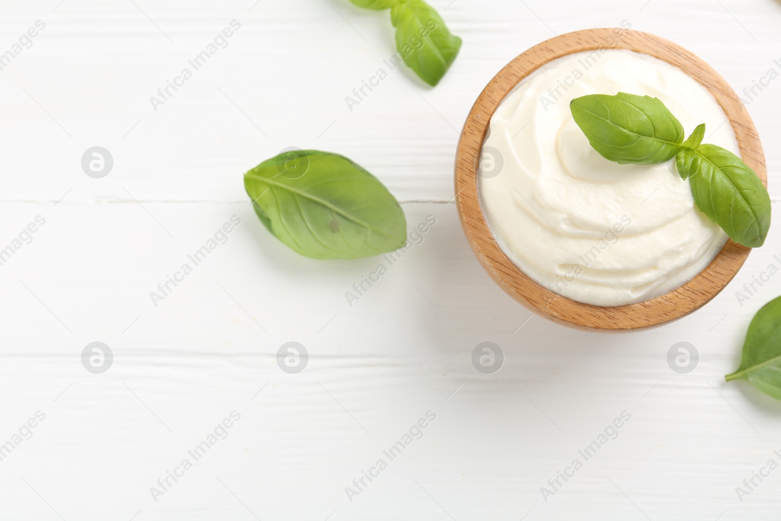 Delicious yogurt in bowl and basil on white wooden table, flat lay. Space for text Photo of Delicious yogurt in bowl and basil on white wooden table, flat lay. Space for text