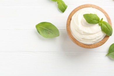 Photo of Delicious yogurt in bowl and basil on white wooden table, flat lay. Space for text