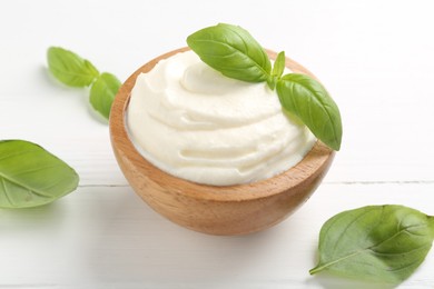 Photo of Delicious yogurt in bowl and basil on white wooden table, closeup