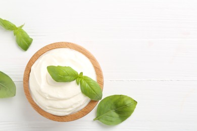 Photo of Delicious yogurt in bowl and basil on white wooden table, flat lay. Space for text