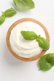 Photo of Delicious yogurt in bowl and basil on white wooden table, flat lay