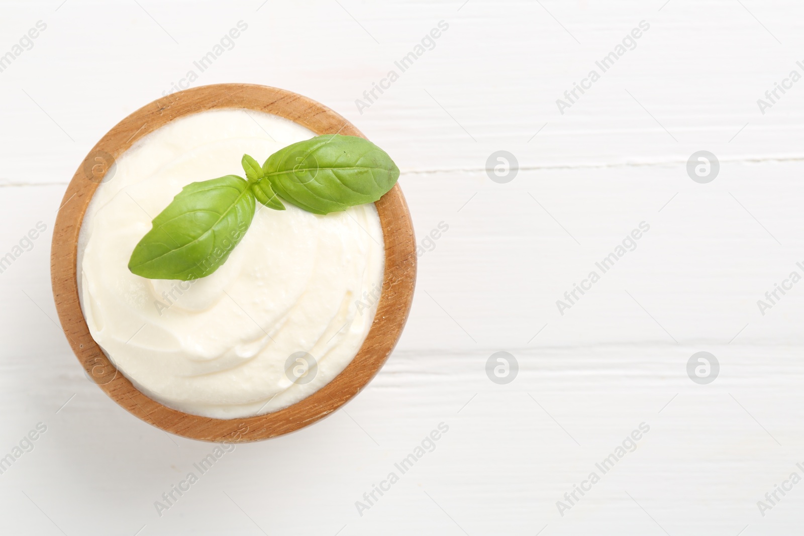 Photo of Delicious yogurt with basil in bowl on white wooden table, top view. Space for text