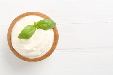 Photo of Delicious yogurt with basil in bowl on white wooden table, top view. Space for text