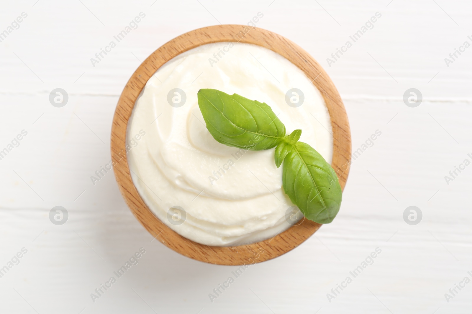 Delicious yogurt with basil in bowl on white wooden table, top view Photo of Delicious yogurt with basil in bowl on white wooden table, top view