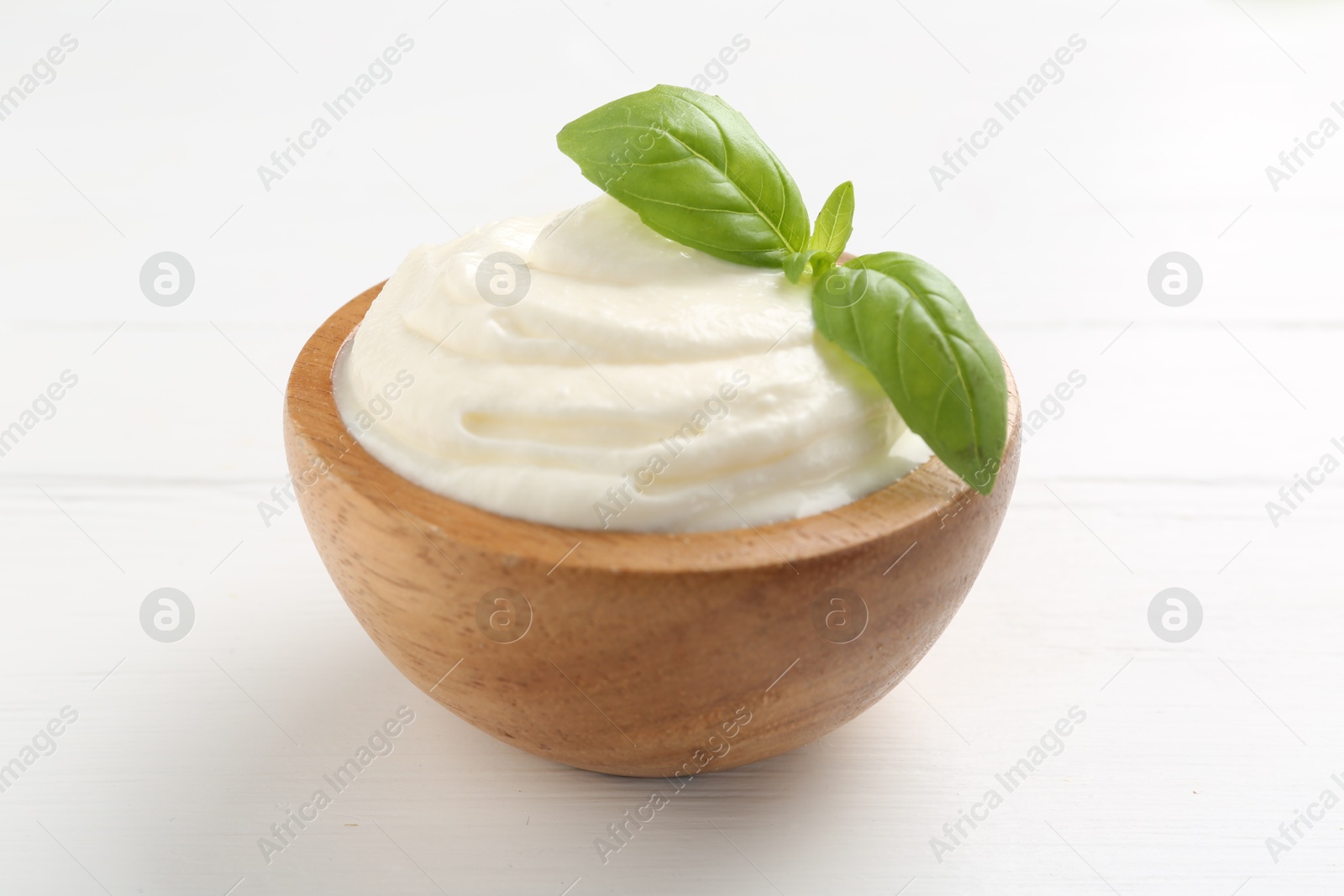 Photo of Delicious yogurt with basil in bowl on white wooden table, closeup