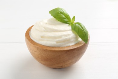 Photo of Delicious yogurt with basil in bowl on white wooden table, closeup