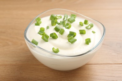 Photo of Delicious yogurt with green onions in bowl on wooden table, closeup