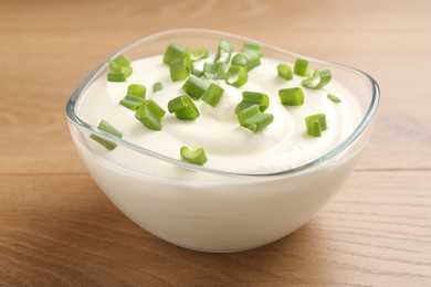 Photo of Delicious yogurt with green onions in bowl on wooden table, closeup