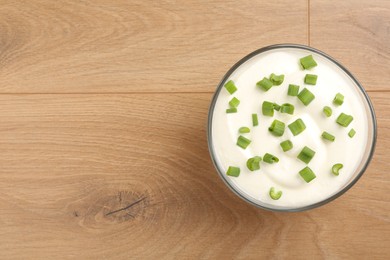 Photo of Delicious yogurt with green onions in bowl on wooden table, top view. Space for text