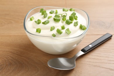 Photo of Delicious yogurt in bowl, green onions and spoon on wooden table, closeup