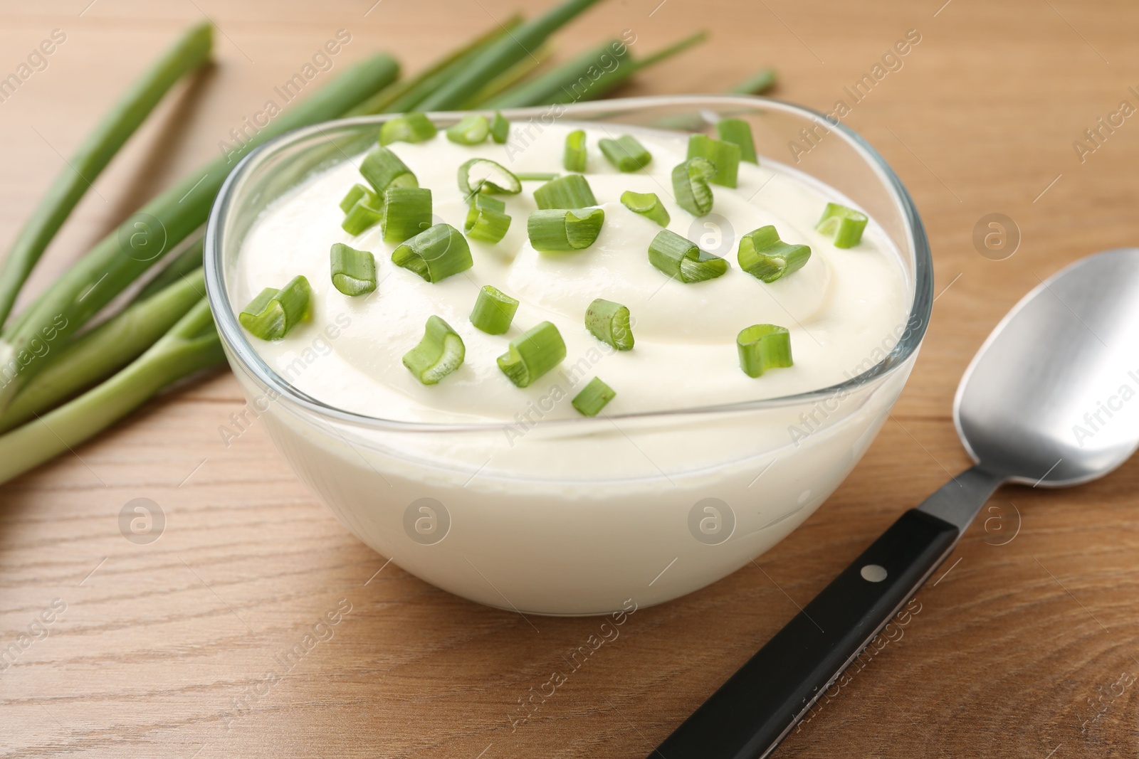 Delicious yogurt in bowl, green onions and spoon on wooden table, closeup Photo of Delicious yogurt in bowl, green onions and spoon on wooden table, closeup