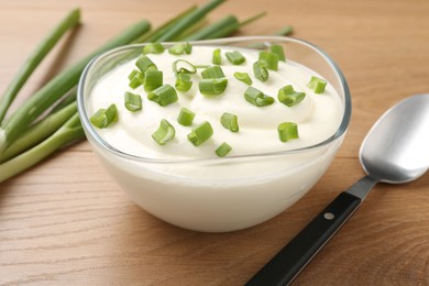 Photo of Delicious yogurt in bowl, green onions and spoon on wooden table, closeup