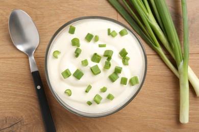 Photo of Delicious yogurt in bowl, green onions and spoon on wooden table, flat lay
