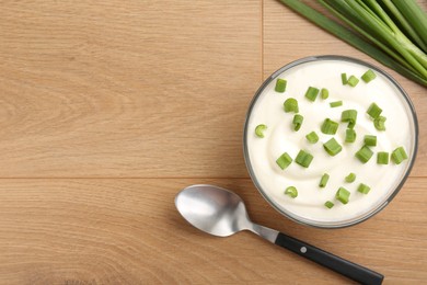 Photo of Delicious yogurt in bowl, green onions and spoon on wooden table, flat lay. Space for text