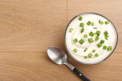 Photo of Delicious yogurt in bowl, green onions and spoon on wooden table, flat lay. Space for text