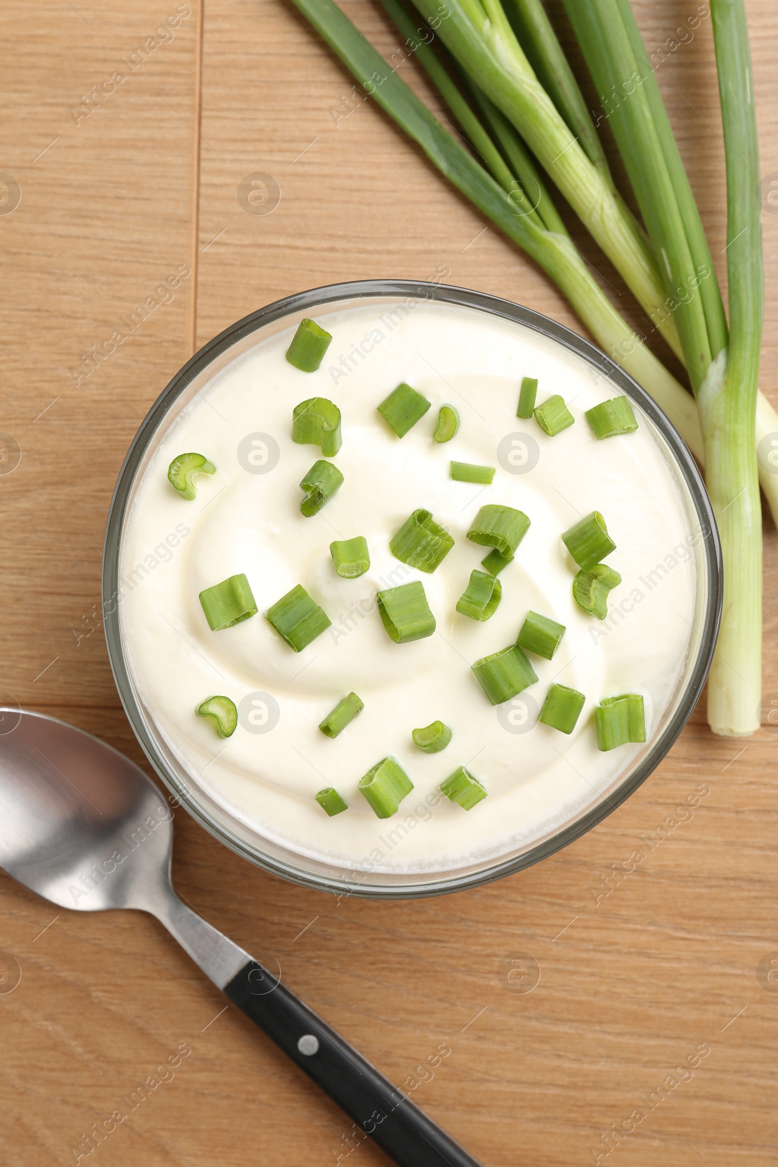 Photo of Delicious yogurt in bowl, green onions and spoon on wooden table, flat lay