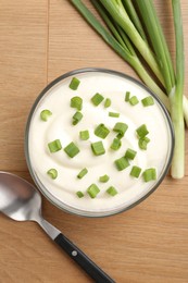 Photo of Delicious yogurt in bowl, green onions and spoon on wooden table, flat lay