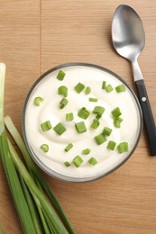 Photo of Delicious yogurt in bowl, green onions and spoon on wooden table, flat lay